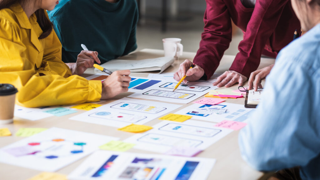 Employees stand and sit around a table reviewing various product designs.